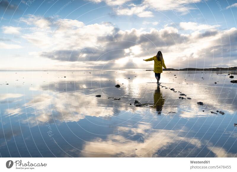 Woman walking amidst sea with reflection in Hvalnes Nature Reserve Beach, Iceland color image colour image outdoors location shots outdoor shot outdoor shots