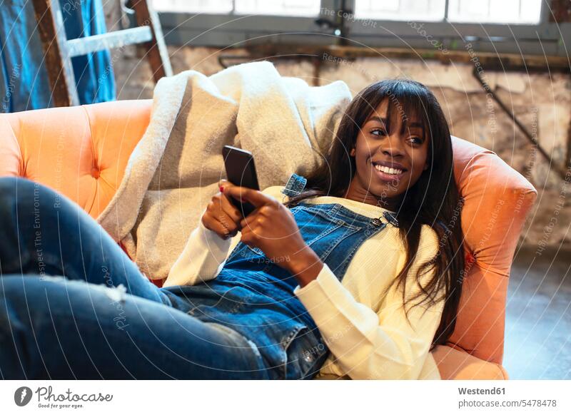 Portrait of smiling woman lying on the couch at home using cell phone Smartphone iPhone Smartphones laying down lie lying down loft lofts smile settee sofa