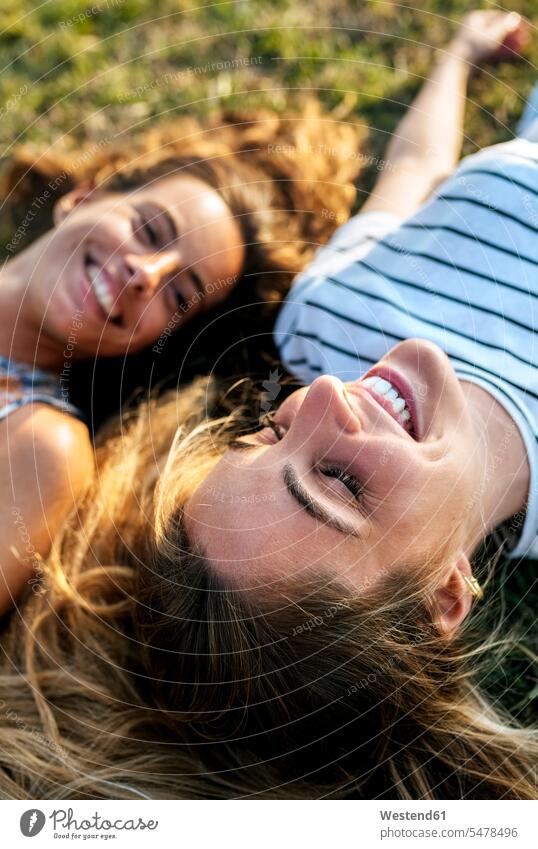 Smiling young woman relaxing with sister on field color image colour image outdoors location shots outdoor shot outdoor shots Spain smiling smile day