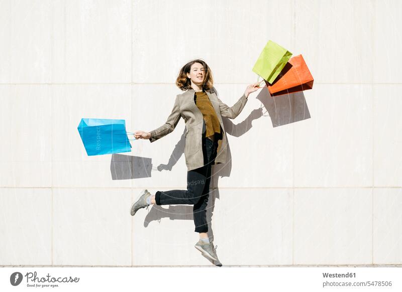 Cheerful woman with shopping bags jumping at a wall portrait portraits cheerful gaiety Joyous glad Cheerfulness exhilaration merry gay females women Leaping
