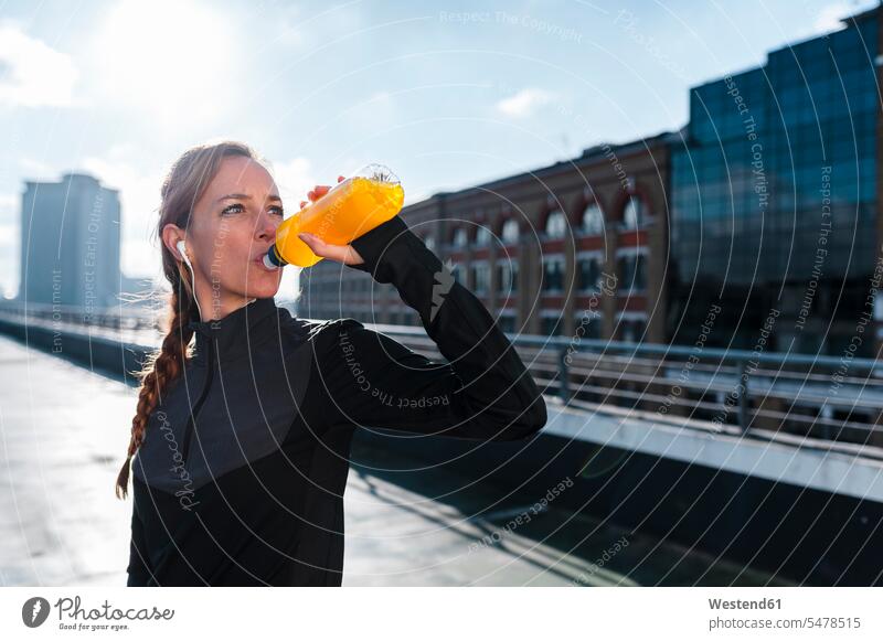 Female athlete having drink while standing on rooftop against sky during sunny day color image colour image outdoors location shots outdoor shot outdoor shots