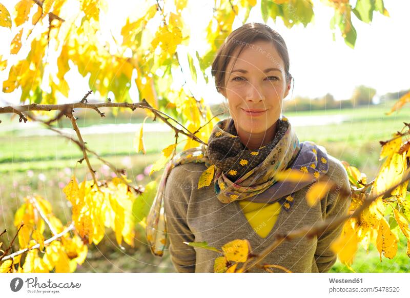 Portrait of woman at twigs with autumn leaves looking at camera scarfs scarves smile delight enjoyment Pleasant pleasure indulgence indulging savoring happy