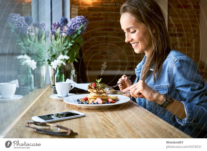 Smiling young woman eating pancakes in cafe smiling smile females women Pancake Pancakes Adults grown-ups grownups adult people persons human being humans