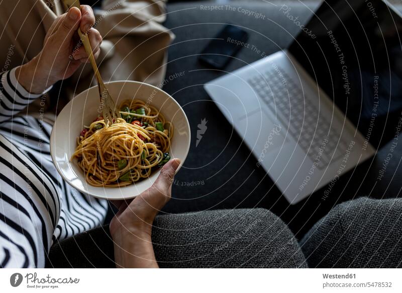 Mature woman with laptop eating homemade pasta dish on couch at home human human being human beings humans person persons celibate celibates singles