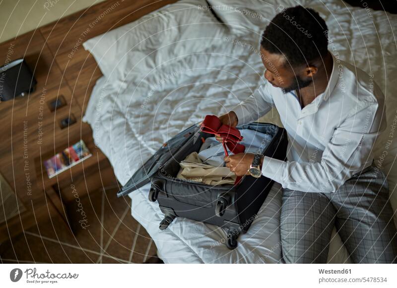 Businessman sitting on bed in hotel room packing his suitcase business life business world business person businesspeople Business man Business men Businessmen