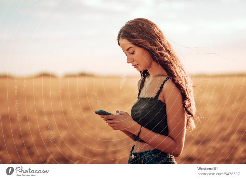Young woman with long hair using mobile phone while standing on landscape against sky color image colour image Spain leisure activity leisure activities
