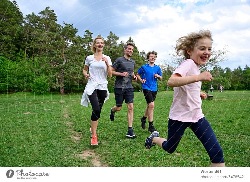 Cheerful family running on meadow against trees in forest color image colour image Germany wood woods forests nature natural world the natural world outdoors