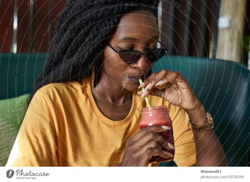 Young woman with dreadlocks drinking a smoothie in a cafe African descent black coloured health awareness health-conscious day daylight shot daylight shots