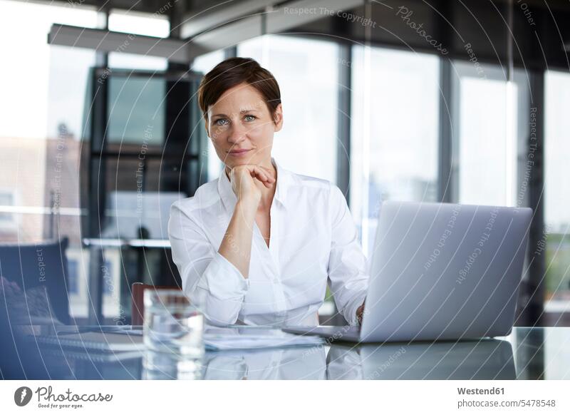 Portrait of confident businesswoman sitting at glass table in office with laptop confidence businesswomen business woman business women portrait portraits