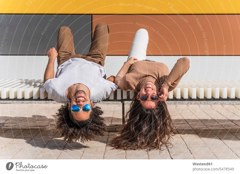 Couple with sunglasses, relaxing on bench, lying on back, heads hanging down associate associates partner partners partnerships artists benches Eye Glasses