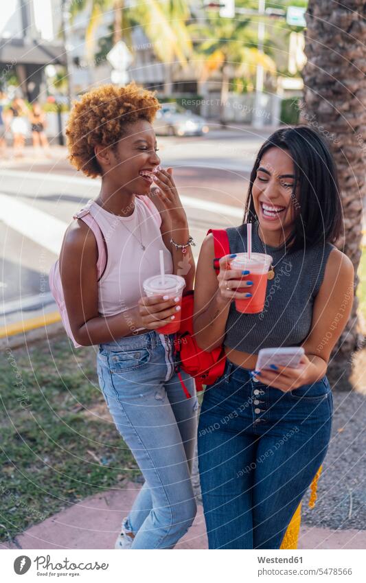 USA, Florida, Miami Beach, two happy female friends with cell phone and soft drink in the city mobile phone mobiles mobile phones Cellphone cell phones town