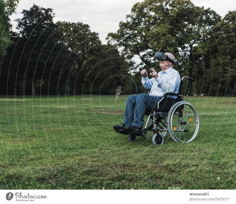 Senior man sitting in wheelchair in a park using Virtual Reality Glasses wheelchairs discover discovering relax relaxing smile look seeing view viewing Seated