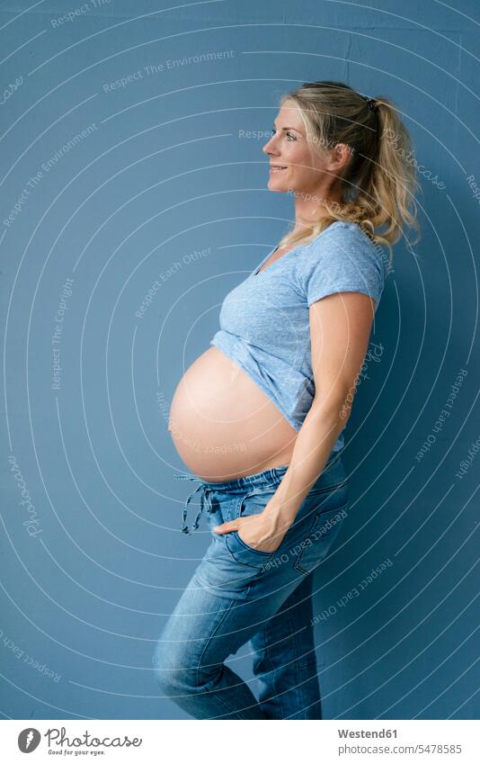 Smiling pregnant woman standing at blue wall walls Pregnant Woman females women colour colours Adults grown-ups grownups adult people persons human being humans