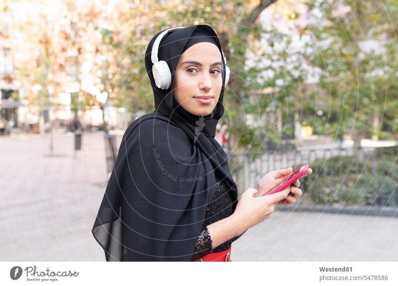 Portrait of young beautiful woman wearing hijab and headphones using smart phone outdoors location shots outdoor shot outdoor shots day daylight shot