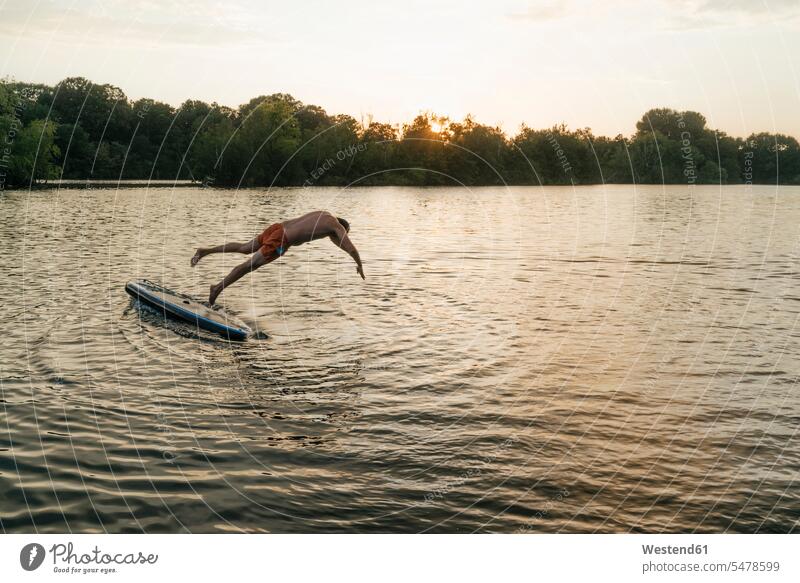 Man jumping from SUP board on a lake at sunset swimming Paddleboard standup paddleboard paddle board Paddleboards sunsets sundown man men males lakes Leaping