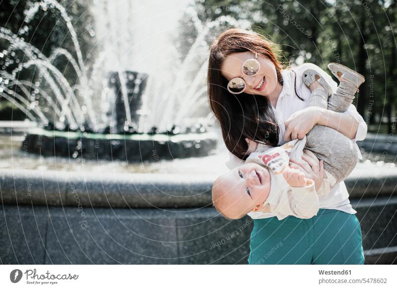 Mother playing with her baby boy near a fountain delight enjoyment Pleasant pleasure smile community human human being human beings humans person persons