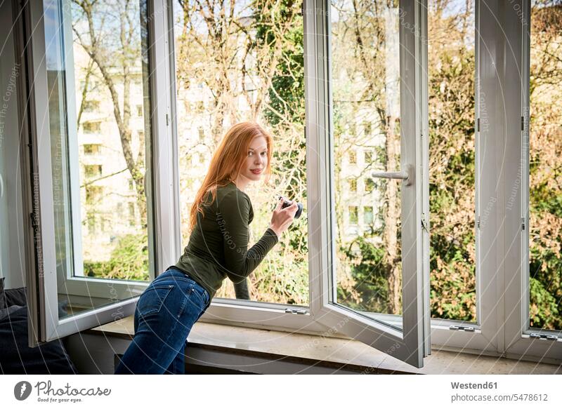 Portrait of smiling redheaded woman leaning out of window camera cameras red hair red hairs red-haired females women windows people persons human being humans