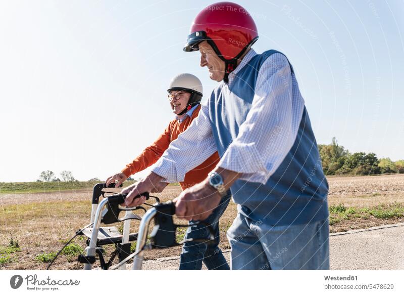 Two old friends wearing safety helmets, competing in a wheeled walker race competition country road rural road rural roads country roads Safety Helmet