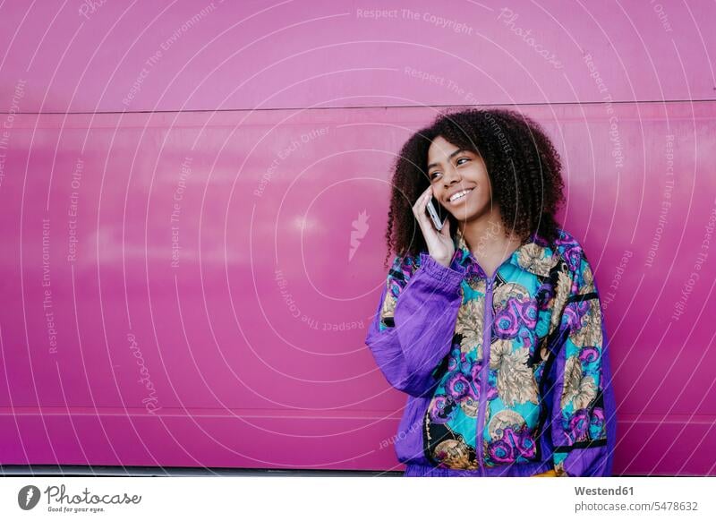 Smiling woman talking on the phone, pink wall in the background coat coats jackets telecommunication phones telephone telephones cell phone cell phones