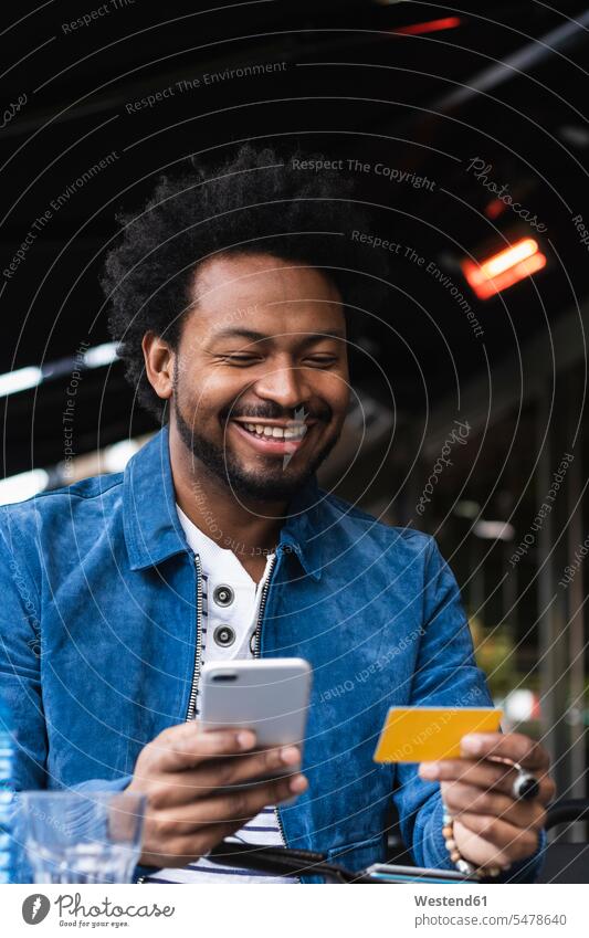 Smiling man using credit card and smart phone for paying at sidewalk cafe color image colour image Spain leisure activity leisure activities free time