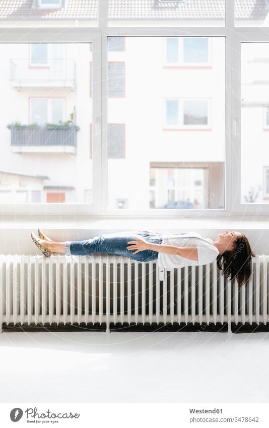 Woman lying on heater in front of window windows pretty Prettiness woman females women hovering floating radiator laying down lie lying down Adults grown-ups