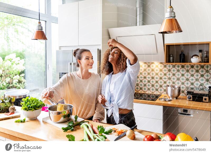 Businesswoman with colleague tasting spaghetti in office kitchen color image colour image indoors indoor shot indoor shots interior interior view Interiors day