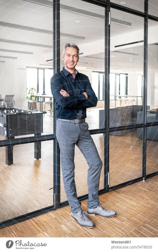 Businessman leaning on glass wall in his office, with arms crossed human human being human beings humans person persons caucasian appearance caucasian ethnicity