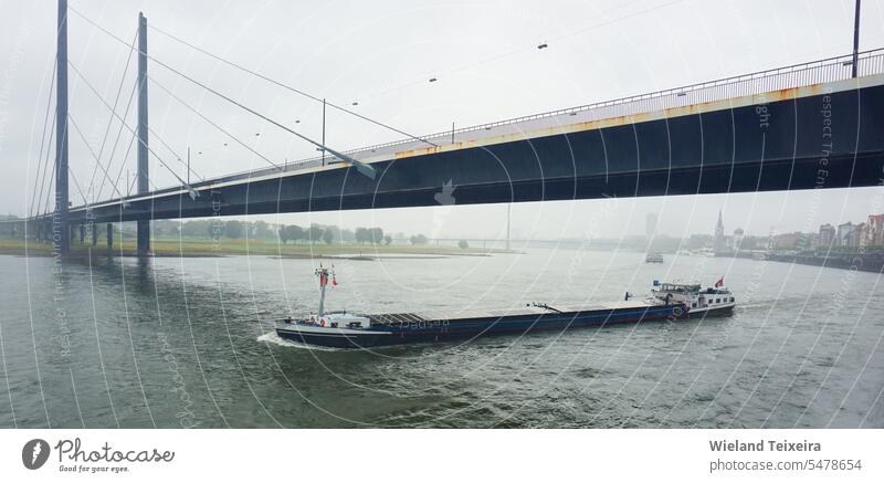 A bridge over the Rhine on a rainy day. A loaded barge sails under the bridge germany grey sky water landscape weather nature outdoor nobody europe transport