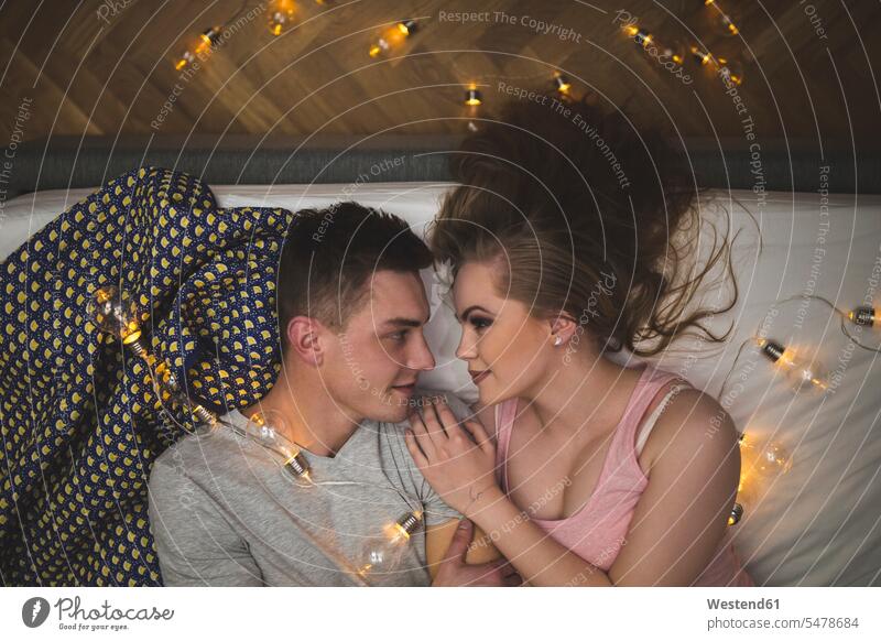 Romantic young couple cuddling in bed with fairy lights beds lying laying down lie lying down romantic lyrical Romance snuggle cuddle snuggling string light