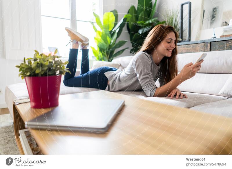 Smiling woman lying on couch with cell phone human human being human beings humans person persons caucasian appearance caucasian ethnicity european adult