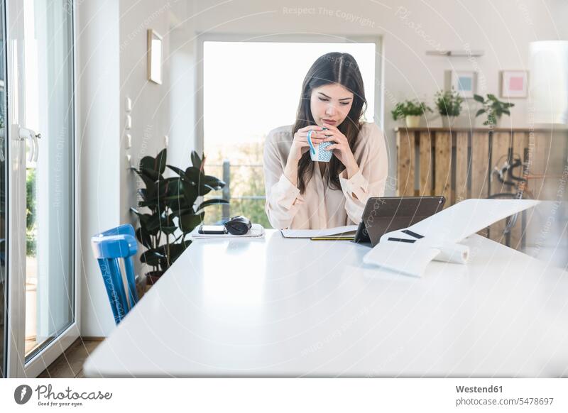 Young woman sitting at table at home using tablet Seated females women Table Tables Adults grown-ups grownups adult people persons human being humans