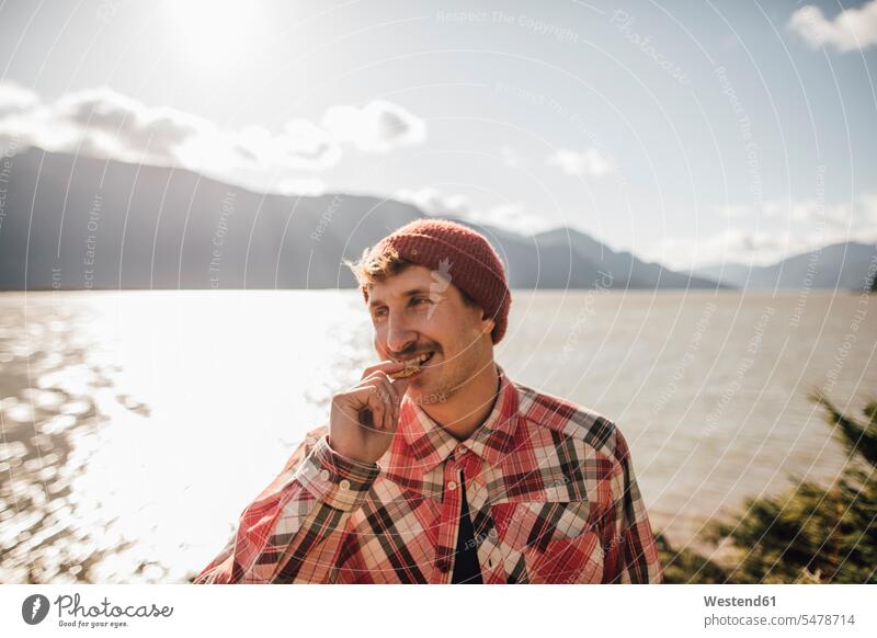Canada, British Columbia, portrait of smiling man eating a cookie smile Biscuit Cookie Cooky Cookies Biscuits portraits men males lake lakes Pastry Pastries