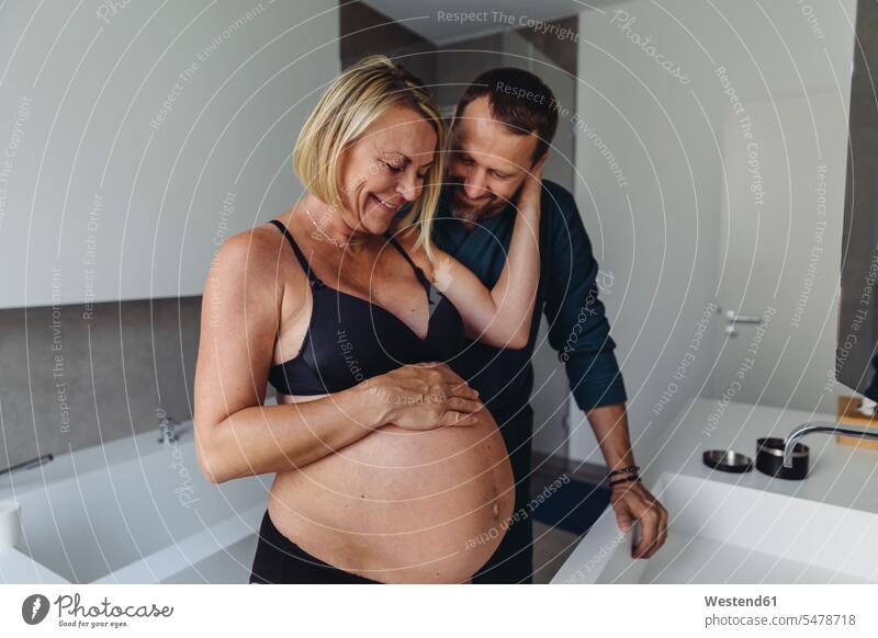 Happy mature pregnant couple watching expectant mother’s belly in bathroom Domestic Bathroom bath room Pregnant Woman looking eyeing bellies abdomen