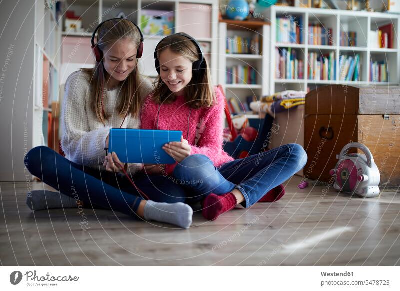 Siblings playing at home with their digital tablets, sitting on ground Germany childhood toothy smile big smile open smile laughing togetherness wireless