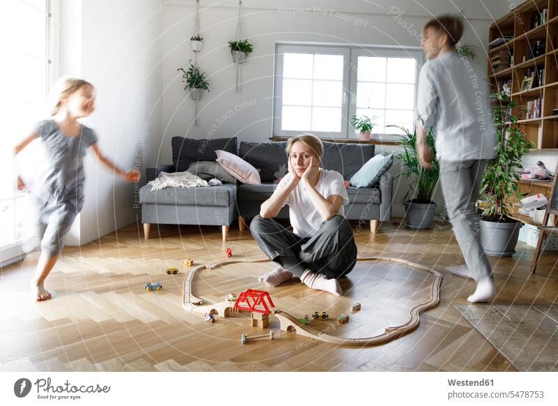 Stressed out mother sitting in the middle of toys, while children are running around her human human being human beings humans person persons