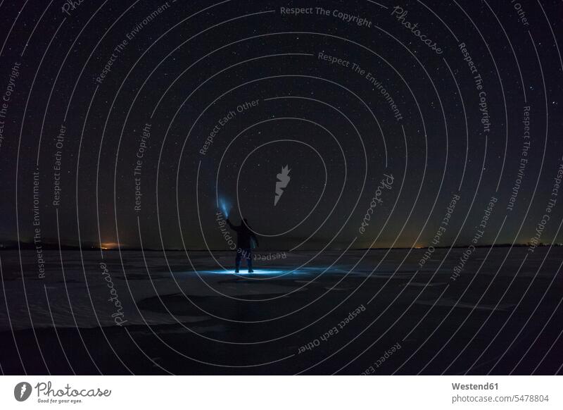 Russia, Amur Oblast, silhouette of man with blue ray standing on frozen Zeya River at night under starry sky men males beams of light beam of light rays