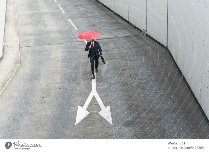 Businessman with red umbrella walking on road marking color image colour image outdoors location shots outdoor shot outdoor shots day daylight shot