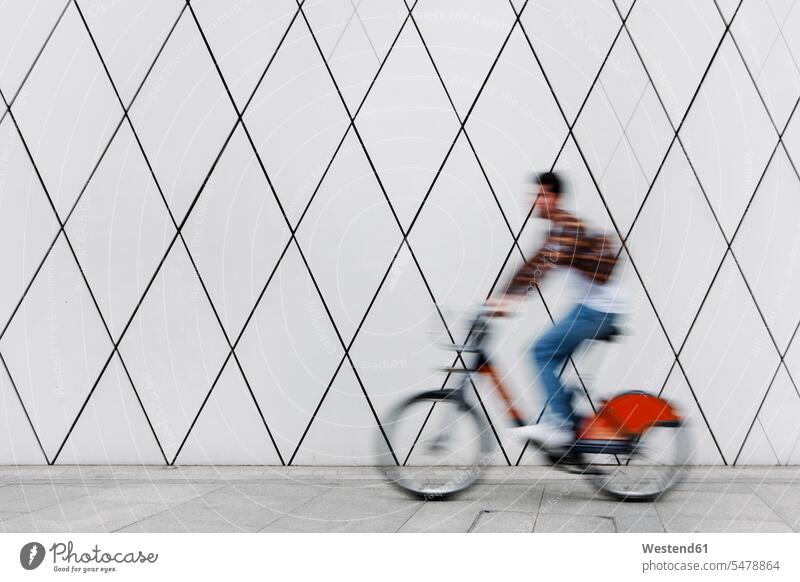 Young man cycling on footpath by wall color image colour image outdoors location shots outdoor shot outdoor shots day daylight shot daylight shots day shots