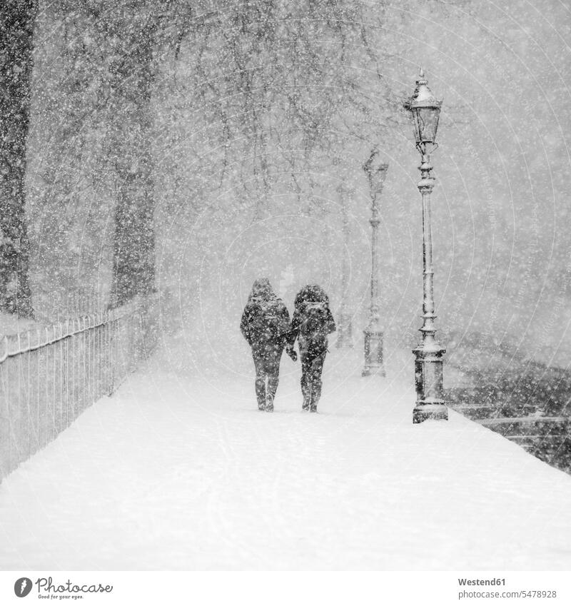 Couple walking together in snow-covered park during heavy snowfall outdoors location shots outdoor shot outdoor shots day daylight shot daylight shots day shots