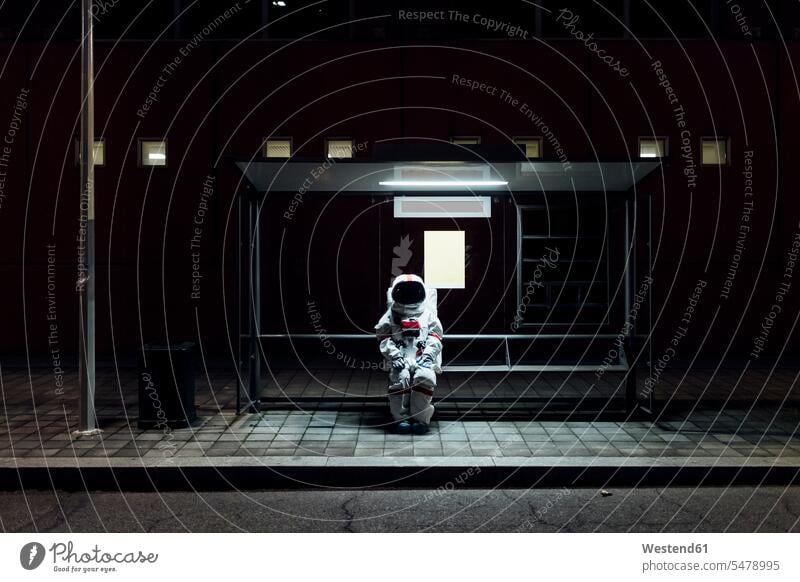 Female astronaut sitting at bus stop during night color image colour image outdoors location shots outdoor shot outdoor shots astronauts spaceman spacemen