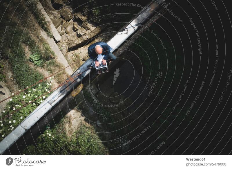 Drone shot of bald businessman using laptop while sitting on old pipes color image colour image Austria outdoors location shots outdoor shot outdoor shots day
