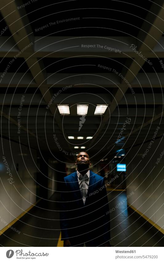 Young male professional looking up while standing under illuminated light in subway color image colour image Spain Businessman Businessmen Business man