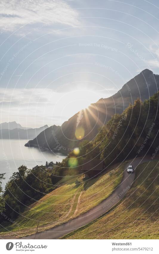 Switzerland, Gersau, Schwyz, Car driving along winding road at sunset with Lake Lucerne in background outdoors location shots outdoor shot outdoor shots sunsets