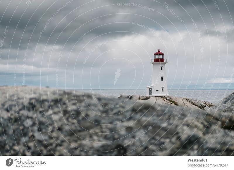 Peggys Point Lighthouse on rock formation by sea against cloudy sky, Nova Scotia, Canada color image colour image outdoors location shots outdoor shot