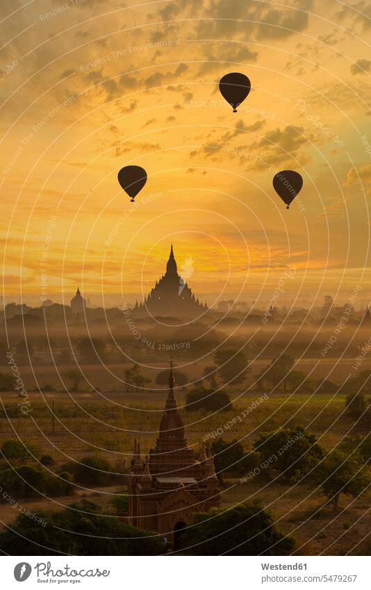 Myanmar, Mandalay Region, Bagan, Silhouettes of hot air balloons flying over ancient temples at foggy dawn outdoors location shots outdoor shot outdoor shots