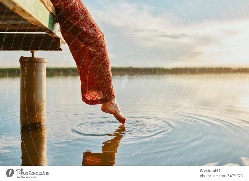 Woman sitting on jetty at a lake at sunset touching the water with her foot human human being human beings humans person persons caucasian appearance