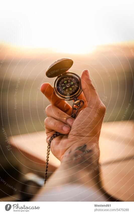 Young man's hand holding navigational compass color image colour image outdoors location shots outdoor shot outdoor shots sunset sunsets sundown atmosphere