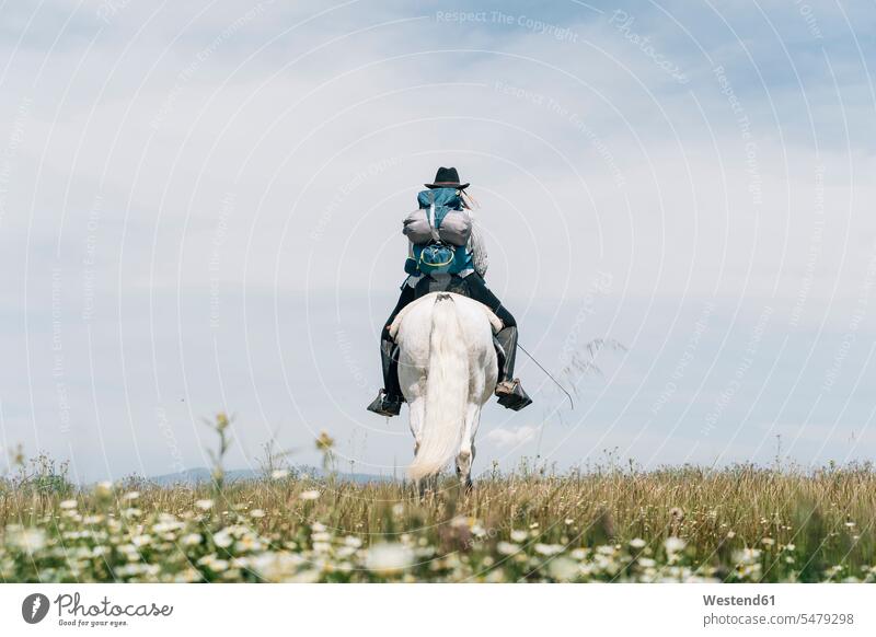 Young woman wearing backpack riding horse on meadow during sunny day outdoors location shots outdoor shot outdoor shots Spain color image colour image