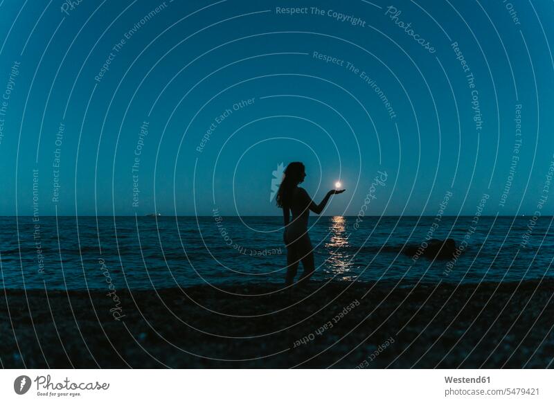 Optical illusion of silhouette woman holding moon over sea against clear sky at night color image colour image leisure activity leisure activities free time