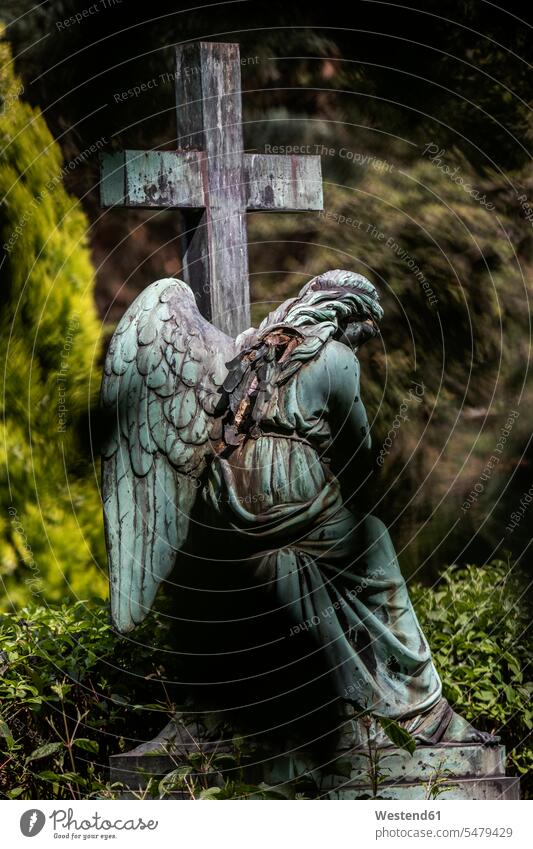 Weathered statue of angel sitting beside cross in cemetery outdoors location shots outdoor shot outdoor shots day daylight shot daylight shots day shots daytime